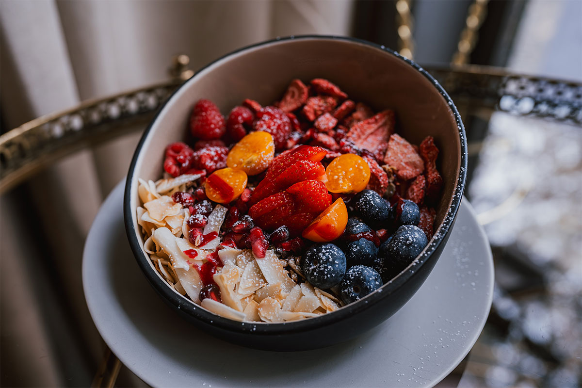 Köstlich aussehendes Früchte-Müsli mit Erdbeeren, Blaubeeren, Himbeeren, Mandeln, Granatapfel und einer Priese Staubzucker.